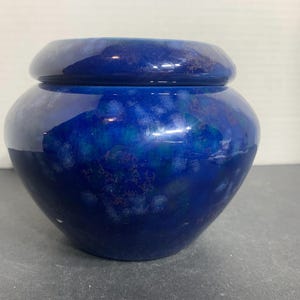 May include: A blue ceramic jar with a lid. The jar has a rounded body and a slightly flared rim. The surface is glossy and features a mottled pattern of dark and light blue hues. A decorative storage container.