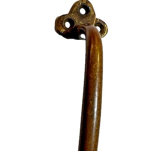 May include: A vintage-style bronze cabinet pull handle. The handle has a curved, cylindrical grip and is attached to decorative, floral-shaped mounting plates with three screw holes each. The metal has a warm, aged patina.