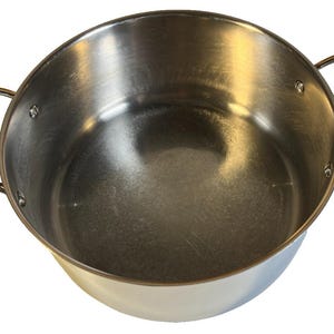 Puede incluir: Olla de cocina de acero inoxidable con dos asas laterales. La olla tiene un cuerpo redondeado y una abertura ancha. Las asas están remachadas a la olla y tienen un diseño curvo. La olla está hecha de metal cepillado brillante.
