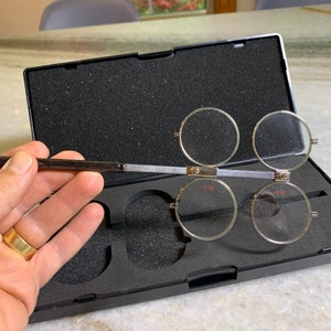 May include: A set of four round magnifying glasses with black frames and a silver metal handle. The glasses are in a black case with a foam interior.