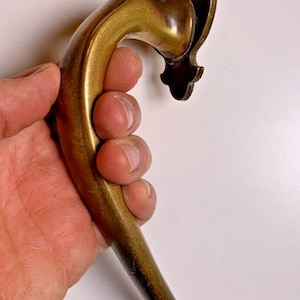 Può includere: Una maniglia per porta in ottone con un design decorativo e ornato. La maniglia è curva e ha una forma lunga e sottile. La maniglia è fissata a una piastra decorativa con un buco della serratura.