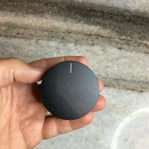 Puede incluir: Un pomo redondo negro con una línea blanca en el centro.