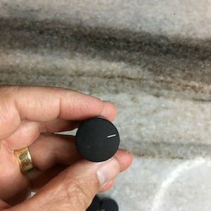 Puede incluir: Primer plano de una perilla negra con una línea blanca. La perilla está siendo sostenida por una mano.