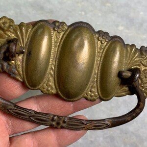 May include: Antique brass drawer pull with an ornate design featuring four oval-shaped accents and floral details. The pull has a curved, metal handle.