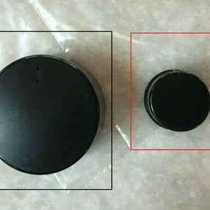 May include: Two black round lids, one larger than the other, on a white surface.