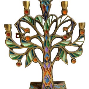 Puede incluir: Una menorá de latón pintada con esmalte de colores vivos, con forma de árbol con cinco portavelas. La menorá tiene un diseño geométrico con detalles en verde, azul, naranja, rojo y morado.