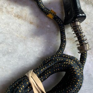 May include: A black and gold electrical cord with a two-prong plug on one end and a three-prong plug on the other end. The cord is coiled and secured with a rubber band.