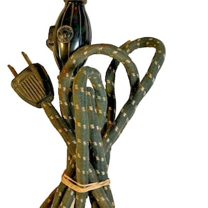 May include: Vintage black and green electrical cord with a plug and a spring-loaded connector. The cord is wrapped in a green fabric with a white dotted pattern. A rubber band holds the cord together.