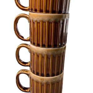 May include: A stack of four brown ceramic mugs with a ribbed design. The mugs are stacked on top of each other, with the handles of each mug visible.
