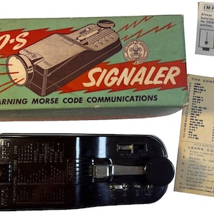 May include: An antique S.O.S. Signaler kit for learning Morse code. The kit includes a black signal device, a box with the words "OFFICIAL S.O.S. SIGNALER" and instructions. The box is green and red. Additional components include a lens and instruction sheets.