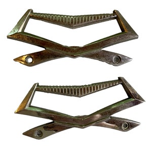 May include: Two vintage chrome car door handles with a diamond pattern. The handles are in the shape of a V and have a hole on each side.