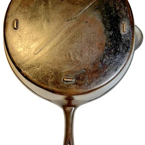 May include: A well-worn cast iron frying pan with a long handle and a circular cooking surface. The pan has a dark, aged appearance, with the numbers 0, 1, and 9 etched on the rim. The handle has a hole for hanging.