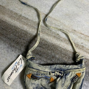 May include: A vintage denim crossbody bag with a light blue and dark blue acid wash pattern. The bag features a zipper pocket, gold-colored accents, and a strap. A tag reads "Liz Thomas".