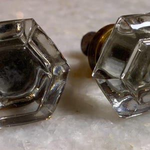 May include: Two clear glass door knobs with a faceted hexagonal design. The knobs are attached to brass bases.