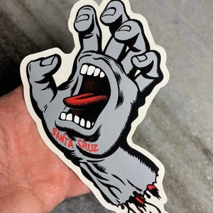 May include: A gray and red screaming hand sticker with the words "Santa Cruz" printed on the wrist.