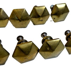 May include: Eight vintage brass cabinet knobs with a geometric, faceted design. The knobs are arranged in two rows of four, showcasing their aged, golden finish and the screw hardware.
