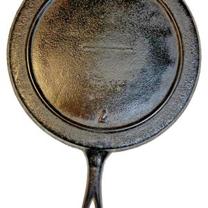May include: A cast iron griddle with a circular cooking surface and a handle with a loop. The griddle is dark grey with a textured surface and a raised rim. The number "7" is visible on the side.