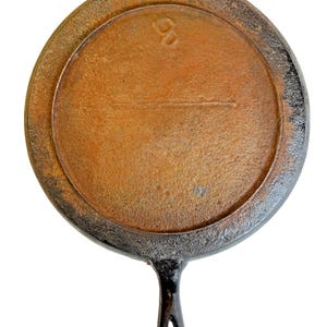 May include: A well-worn, cast iron skillet with a single handle and a circular cooking surface. The skillet has a dark, aged appearance with a rusty brown interior and a black exterior. The handle features a hole for hanging. The number "8" is visible on the surface.