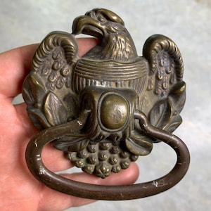 Pode incluir: Puxador de porta antigo de latão com design de águia. A águia está pousada em uma base decorativa com um puxador de anel.