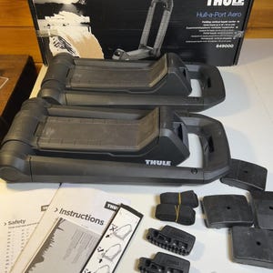 Può includere: Due supporti pieghevoli per kayak Thule Hull-a-Port Aero neri con scatola del marchio, manuali di istruzioni, cinghie nere, staffe di montaggio e un piccolo sacchetto di plastica contenente minuteria metallica e chiavi.