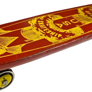 Op de afbeelding: Vintage rood skateboard met gele graphics, inclusief de tekst "USA SKATESHIP APOLLO". Het skateboard heeft zwart-gele wielen en een klassiek, retro design. Het board is ongeveer 76 cm lang.