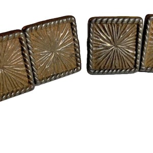 以下が含まれることがあります： 6つの正方形のカフスボタンのセット。各カフスボタンは、金色のテクスチャ加工された太陽光のようなデザインで、銀色のねじれたロープの縁で縁取られています。カフスボタンは、わずかに湾曲した線で接続されています。