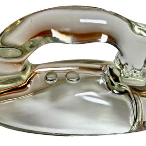 Peut inclure: Un objet décoratif en forme de fer à repasser en verre transparent. La poignée est incurvée vers le haut et la base comporte deux petits détails circulaires. Le verre est réfléchissant, avec des reflets dorés et bruns.