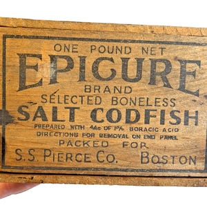 May include: A vintage wooden box, light brown in colour, with the text "EPIGURE BRAND SELECTED BONELESS SALT CODFISH" and "ONE POUND NET". The box is labelled "S.S. PIERCE CO. BOSTON".