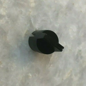 Könnte beinhalten: Schwarzer Kunststoffknopf mit einem einzigen, schrägen Schlitz. Der Knopf ist rund und hat eine glatte Oberfläche.