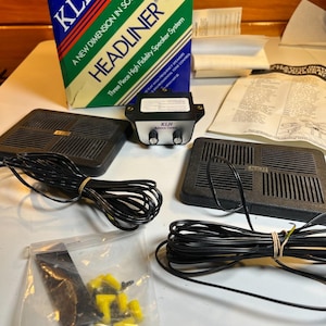 Puede incluir: Sistema de altavoces KLH Headliner vintage. La caja es azul, verde y blanca con detalles en rojo. Incluye dos altavoces negros, una unidad de control y accesorios. La caja dice "A NEW DIMENSION IN SOUND".