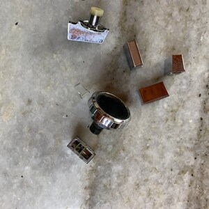 May include: Assortment of vintage chrome and brown plastic knobs and buttons. The knobs have a circular shape with a raised edge and a black center. The buttons are rectangular with a smooth surface.