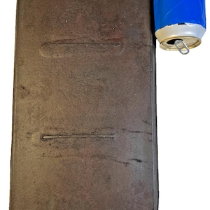Peut inclure: Une plaque de cuisson rectangulaire en fonte brun foncé avec deux poignées. La plaque de cuisson a une surface texturée et deux rainures parallèles. Une canette bleue et argentée est à côté de la plaque.