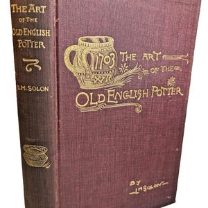 Puede incluir: Un libro antiguo titulado "The Art of the Old English Potter" de L.M. Solon. La portada es de color burdeos oscuro con letras e ilustraciones doradas, incluyendo una jarra decorativa. El lomo es de un tono burdeos más oscuro.