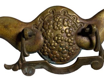 May include: Antique brass cabinet pull with a floral design. The pull has a curved shape and a decorative ring.