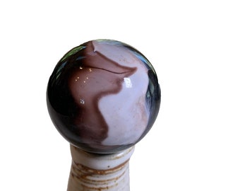 May include: A white ceramic bottle stopper with a brown, white, and black swirl glass orb on top.