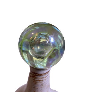 Può includere: Una bottiglia in ceramica con una glassa marrone chiaro e un tappo in marmo di vetro verde. Il marmo ha un motivo a spirale e una finitura iridescente.