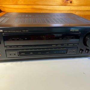 Może przedstawiać: Czarny amplituner stereo audio/wideo Pioneer VSX-452 z cyfrowym wyświetlaczem, dużym pokrętłem głośności, wieloma przyciskami sterującymi, gniazdem słuchawkowym oraz oznaczeniem Dolby Surround Pro Logic na przednim panelu.