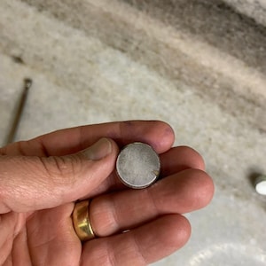 Peut inclure: Un bouton rond de couleur argentée avec une surface texturée.