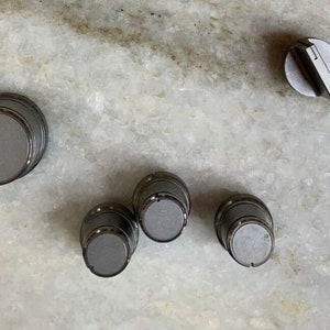 May include: Five gray metal knobs with a single black knob on a white marble surface.