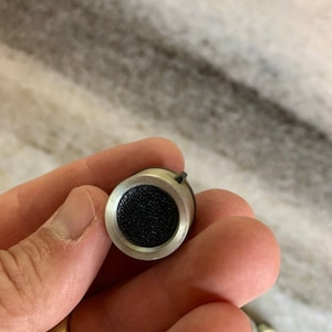 May include: A silver and black microphone capsule with a small, round, black mesh grille.