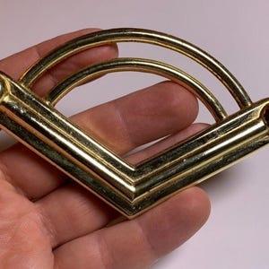 May include: Gold-toned metal drawer pull with a rounded, arched design. The pull has a smooth, polished finish and features two rounded ends.