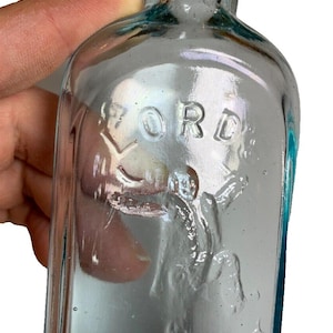 Puede incluir: Una botella de vidrio transparente con una superficie texturizada. La botella tiene las palabras "LORD" y "OPEL DOG" en relieve.