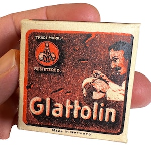 Puede incluir: Una caja de cerillas vintage con un diseño rojo y marrón. La caja de cerillas presenta la palabra "Glattolin" en letras blancas grandes. La caja también incluye el texto "Trade Mark", "Registered" y "Made in Germany."
