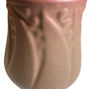 May include: A ceramic mug with a rounded, bulbous shape and a smooth, matte finish in a muted mauve-brown tone. The exterior surface features a subtle, raised vertical relief pattern with a fine crackle glaze texture throughout the entire body.