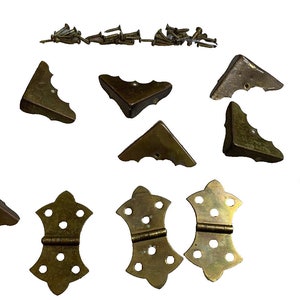 May include: A set of ten brass corner brackets and three brass hinges with decorative scalloped edges. The set includes a pile of small brass screws.