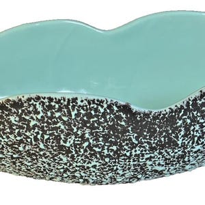 May include: A ceramic serving bowl with an organic shape. The interior is a glossy, light turquoise, contrasting with the textured, speckled exterior in brown and white. The bowl's rim has a wavy design. The bowl is likely 30 cm long.