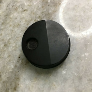 Puede incluir: Un tapón de botella redondo negro con un pequeño agujero en el centro.