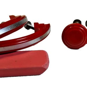 May include: A selection of red and silver cabinet hardware, featuring two curved handles and five round knobs. A pink eraser is also visible. The hardware is suitable for furniture restoration or DIY projects.