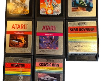 Puede incluir: Una colección de cartuchos de videojuegos Atari 2600 vintage. Los títulos incluyen "Warlords", "Yars' Revenge", "Moon Patrol", "Vanguard", "Phoenix", "Star Voyager", "Atlantis" y "Cosmic Ark". Los cartuchos presentan etiquetas coloridas y carcasas de plástico negro.