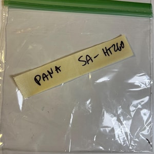 Peut inclure: Un sac en plastique transparent avec une fermeture éclair verte. À l'intérieur, une étiquette en tissu jaune avec le texte manuscrit "PANA SA-HT260" à l'encre noire. Le sac est partiellement transparent.